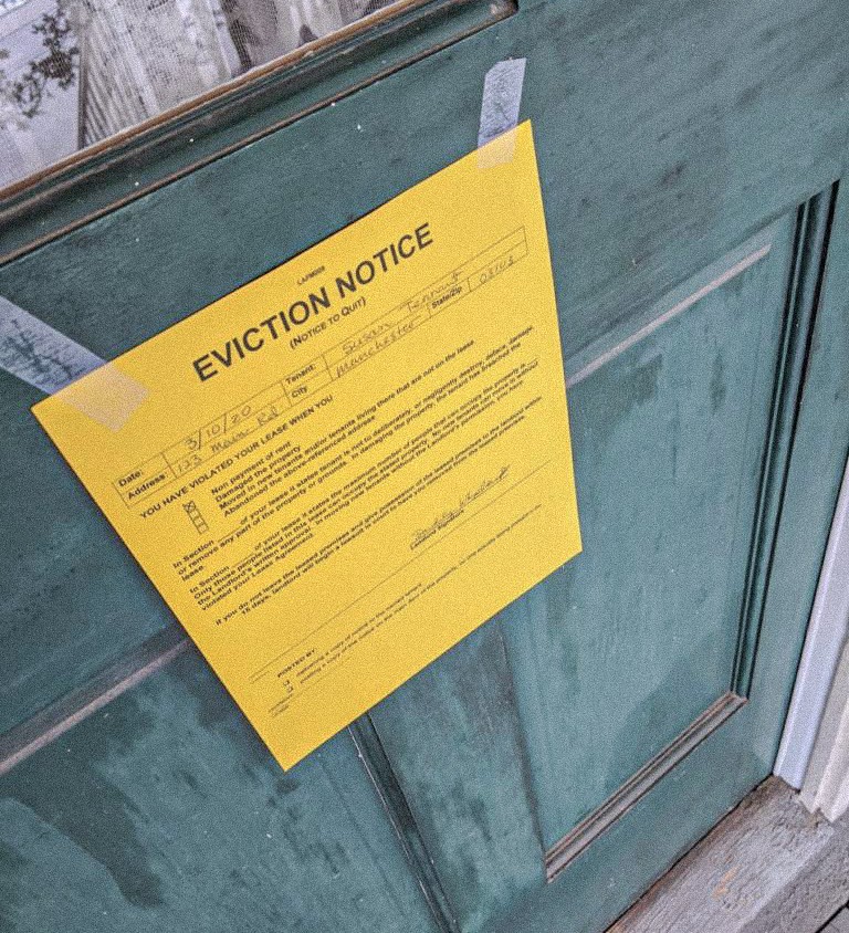 Yellow eviction notice taped to a green door, representing financial hardship, housing instability, and the importance of secure asset and trust protection.