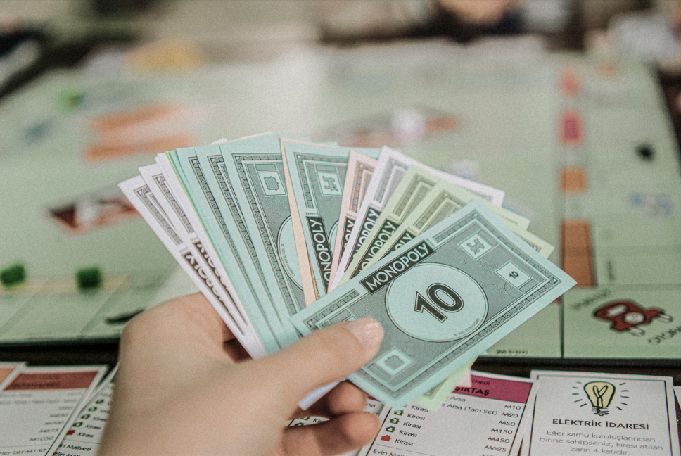 Hand holding Monopoly money over a game board, symbolizing financial strategy, decision-making, and wealth management concepts.