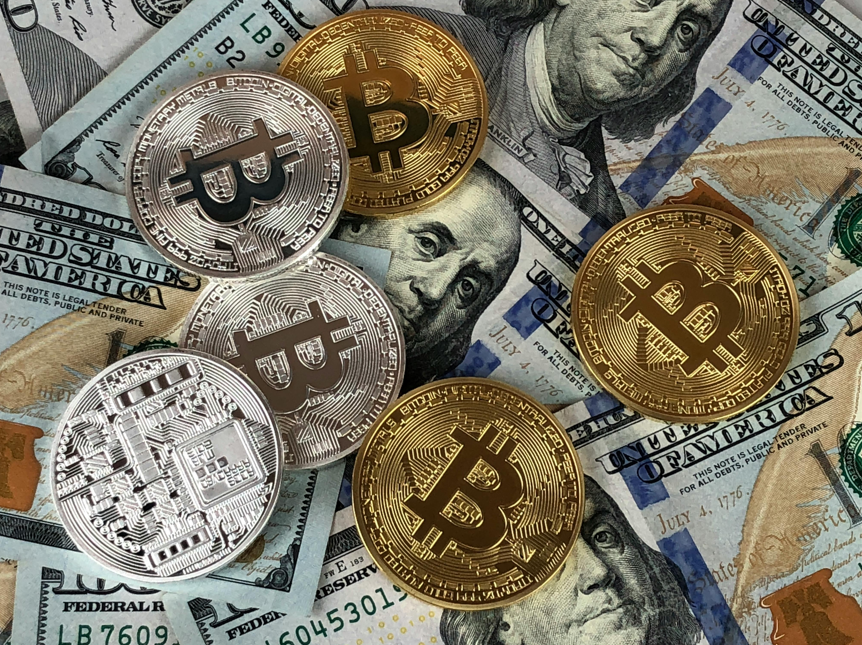 Gold and silver Bitcoin coins placed over U.S. dollar bills, symbolizing the bridge between traditional finance and digital wealth through cryptocurrency.
